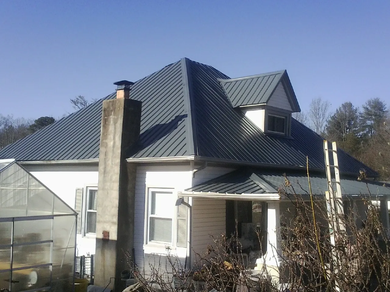 Dark blue standing seam metal roof on a white farmhouse with dormer — Slate & Tile Roof Repair by Roofing Brothers in Grubville