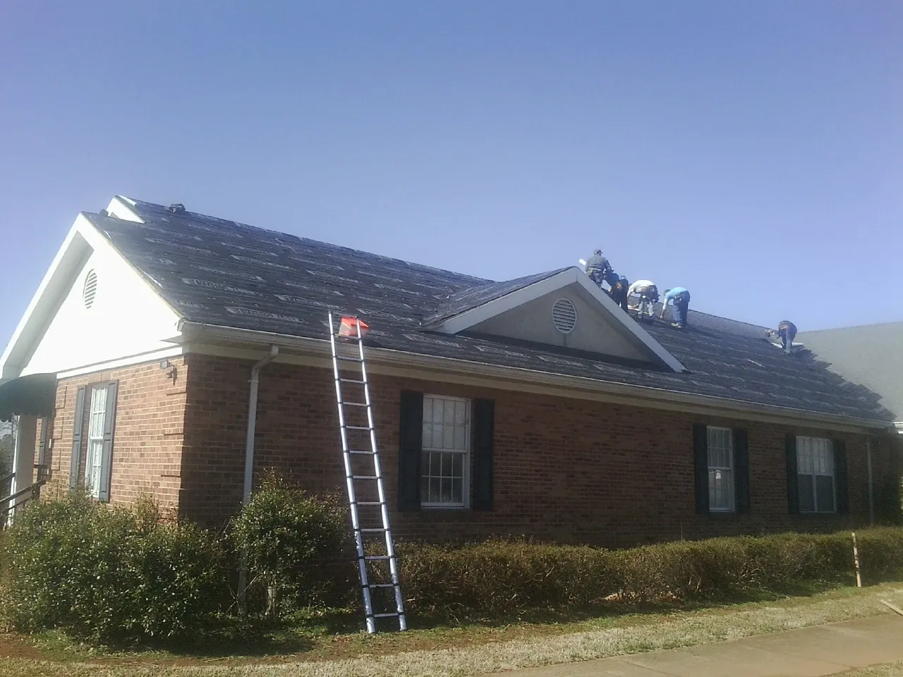 Crew tearing shingles off a brick ranch roof with a ladder set — Emergency Roof Repair work by our crew in Grubville