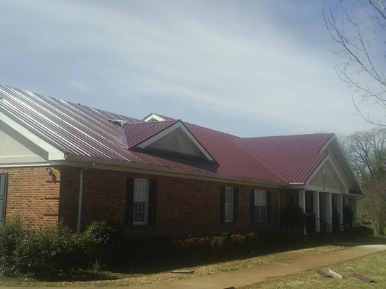 Red metal roof with gabled entries on a long brick building, from a Hail Damage Roof Repair job in Grubville