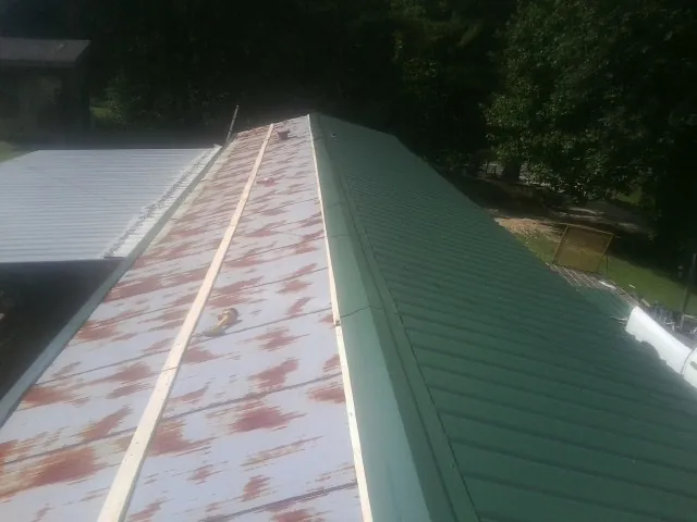 Old rusted panels beside newly installed green metal roofing — Wind Damage Roof Repair by Roofing Brothers in Grubville