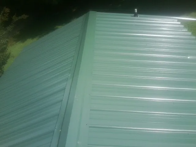 New green metal panels meeting at the ridge of a roof — Flat Roof Repair work by our crew in Grubville