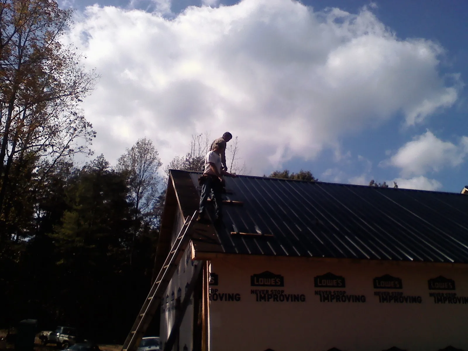 Roofer fastening dark metal panels high against a cloudy sky, from a Roof Inspection job in Grubville