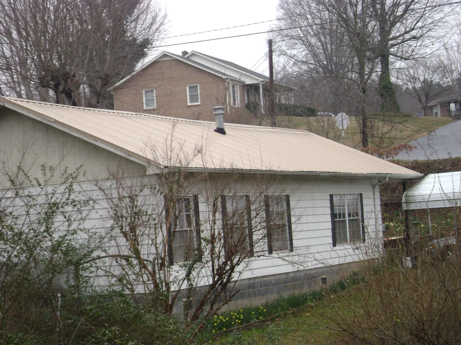Tan metal roof on a white sided house set into a hillside — Commercial Roofing by Roofing Brothers in Grubville